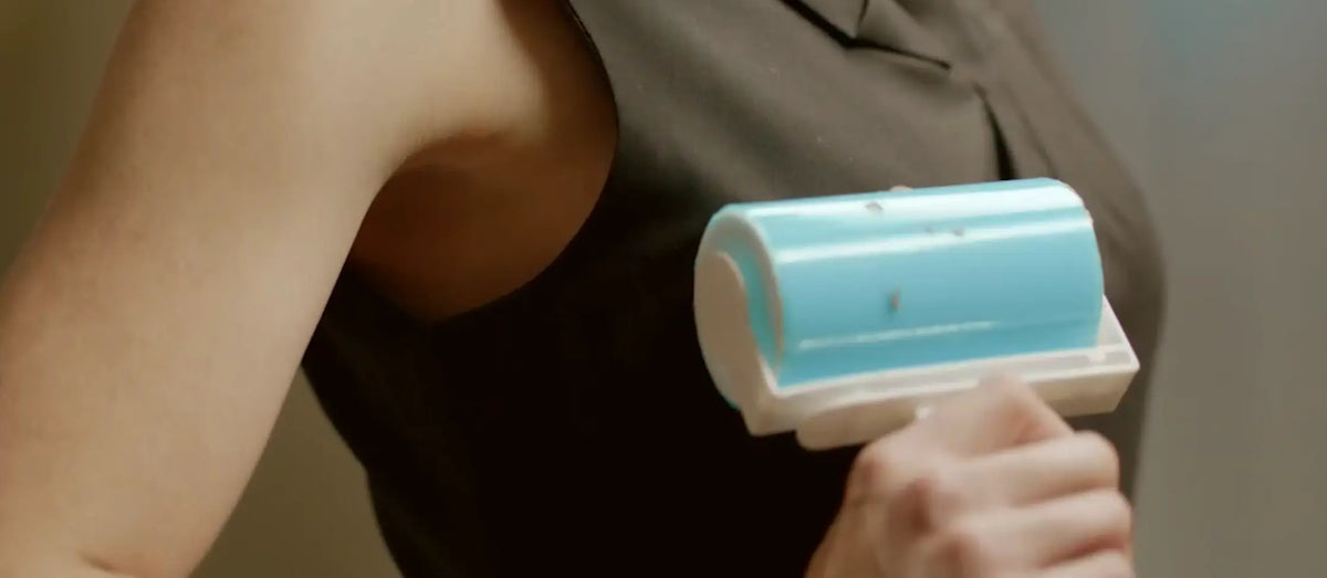 A close-up of a person holding a light blue and white lint roller against their dark sleeveless top.